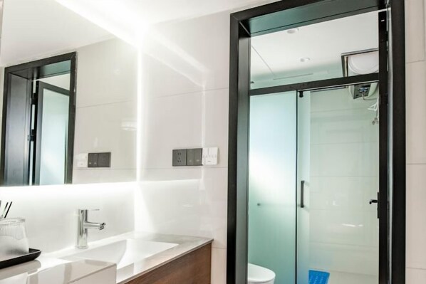 A modern bathroom with a glass-enclosed shower, a white sink with a wooden countertop, and a large mirror above the sink. - Chenjia Courtyard (Guangyuan)