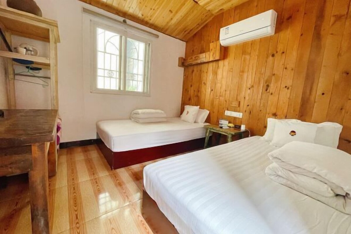 A wooden-paneled room with two beds, a wooden desk, and a window.