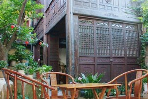 Una puerta de madera tradicional con diseños intrincados, una mesa de madera con sillas y plantas en macetas en un patio.