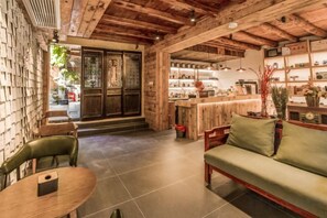 Un interior acogedor con techo de madera, una zona de estar con sofá y sillones, y una barra con estanterías y mostrador.