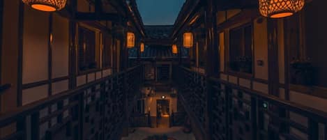 A corridor with lanterns, wooden railings, and a central water feature.
