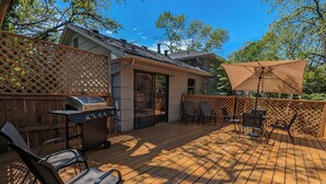 Una terraza de madera con una parrilla, sillas y una mesa.