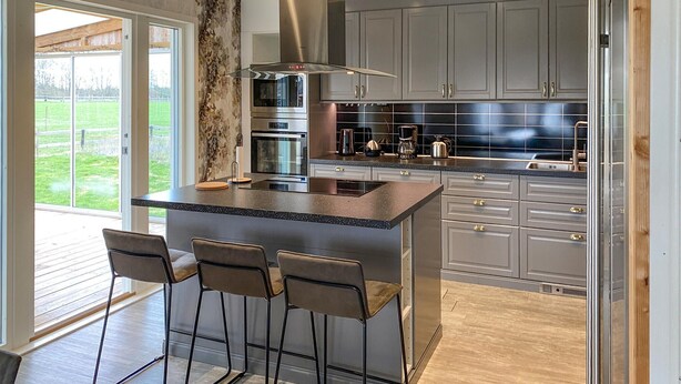 A modern kitchen with a central island, bar stools, stainless steel appliances, and grey cabinetry. - 5 bedroom amazing home in Tingsryd (Tingsryd)
