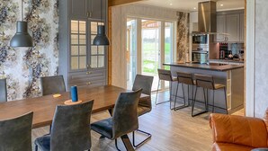 A modern kitchen with a central island, bar stools, and a dining area with a wooden table and chairs. - 5 bedroom amazing home in Tingsryd (Tingsryd)