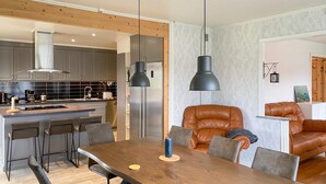 A modern kitchen with grey cabinets, a stainless steel refrigerator, and a built-in oven. There is a dining area with a wooden table and leather chairs. - 5 bedroom amazing home in Tingsryd (Tingsryd)