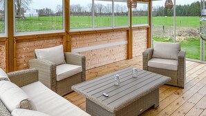 A covered outdoor seating area with wicker furniture and a wooden table, large windows offering views of a green field. - 5 bedroom amazing home in Tingsryd (Tingsryd)