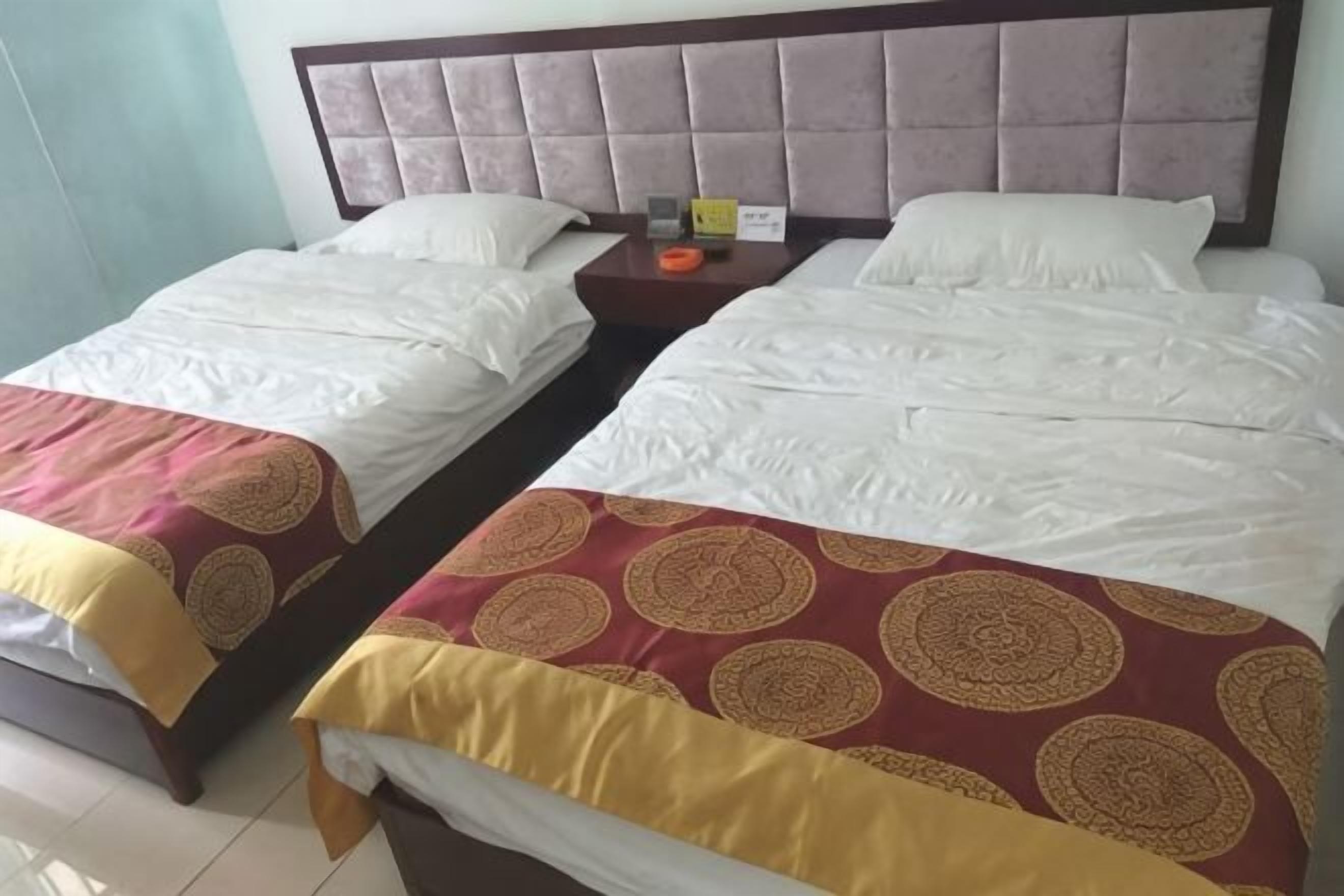 A hotel room with two beds, a nightstand, and a headboard.