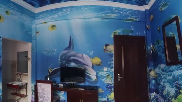 Une pièce décorée d’une fresque murale aux motifs bleus évoquant l’océan, avec une télévision et une porte en bois.
