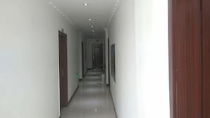 Un couloir étroit aux murs blancs, avec une porte en bois sur la droite et une porte au fond.
