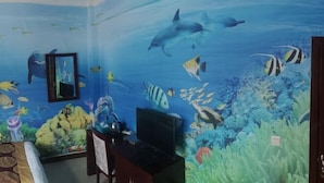 Une pièce décorée d’une fresque représentant un paysage sous-marin, avec un lit, un bureau doté d’un ordinateur et un téléviseur.