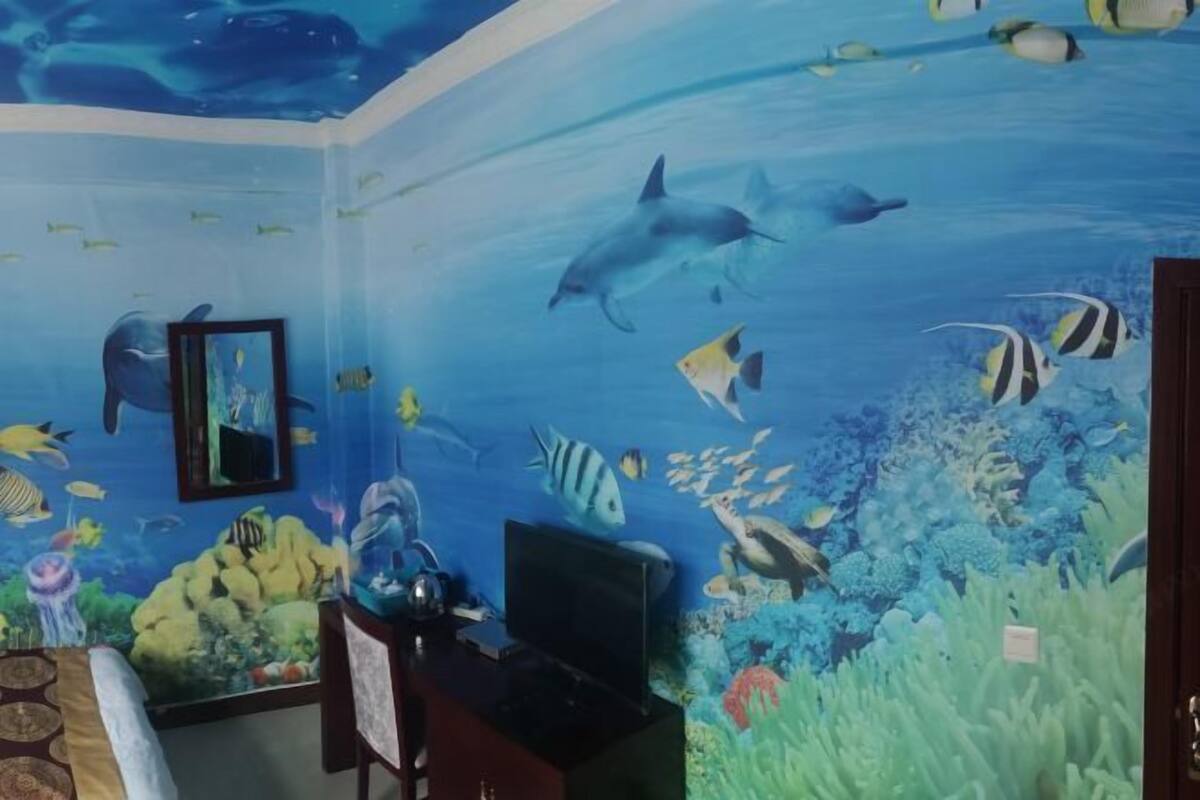 Een kamer met een muurschildering van een onderwaterdecor, een bed, een bureau met een computer en een televisie.