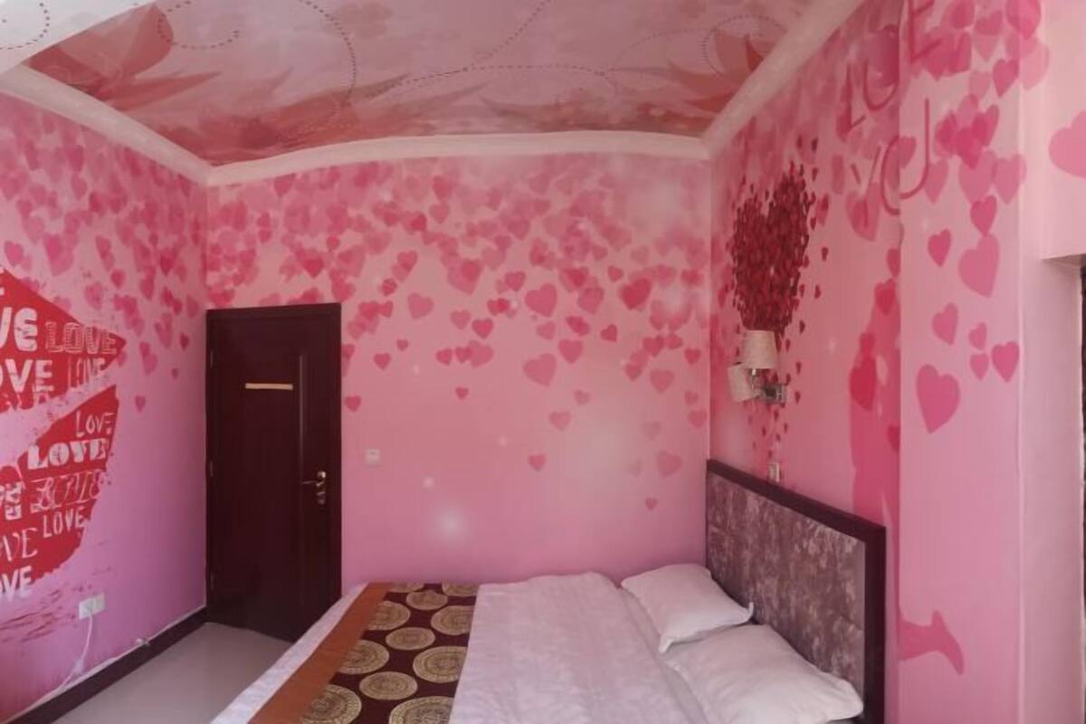 Een slaapkamer in roze tinten met een bed, een deur en een hartjes-versierde muur.