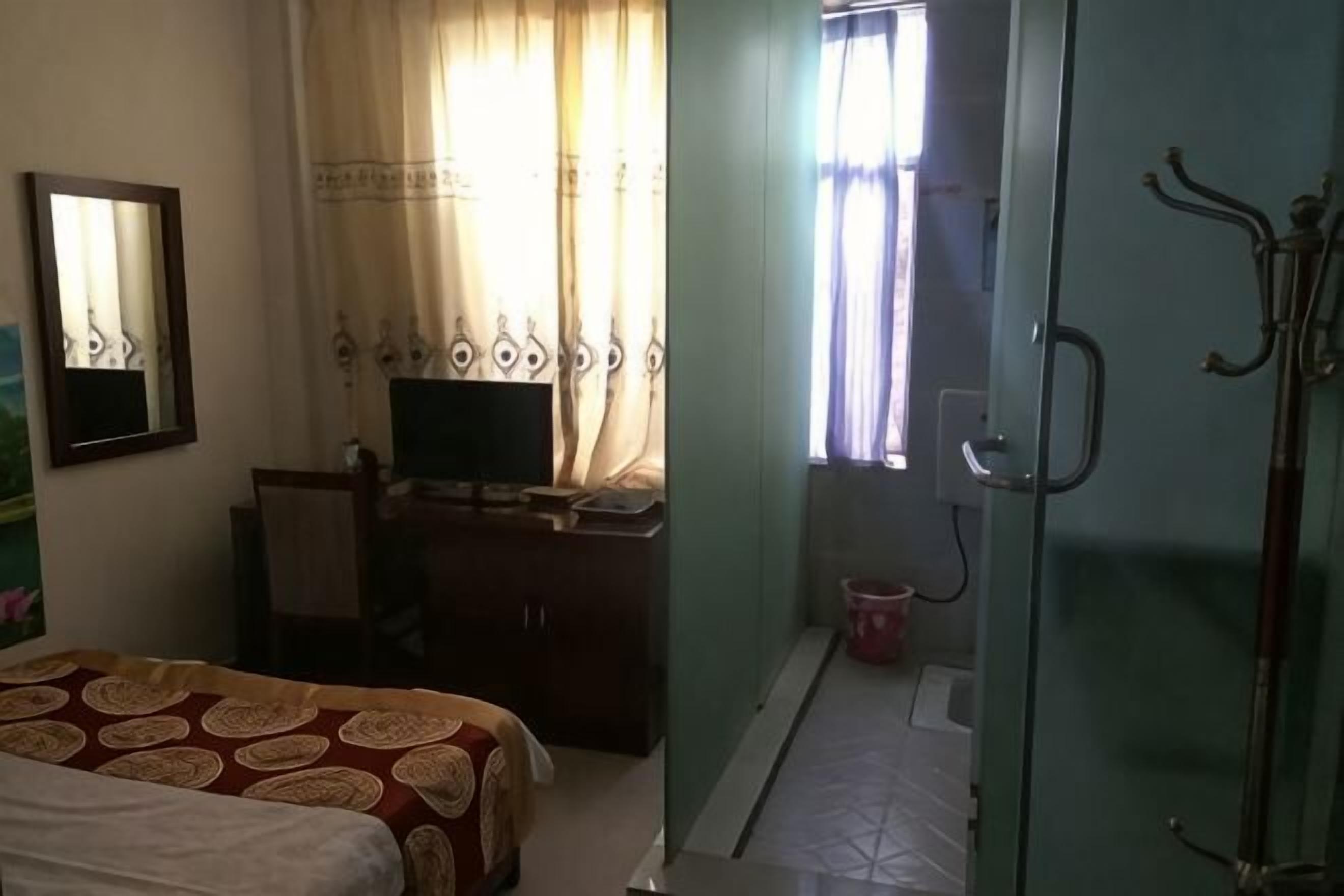 Ein Schlafzimmer mit einem Bett, einem Schreibtisch mit Computer, einem Kleiderschrank und einem Fenster mit Vorhängen.
