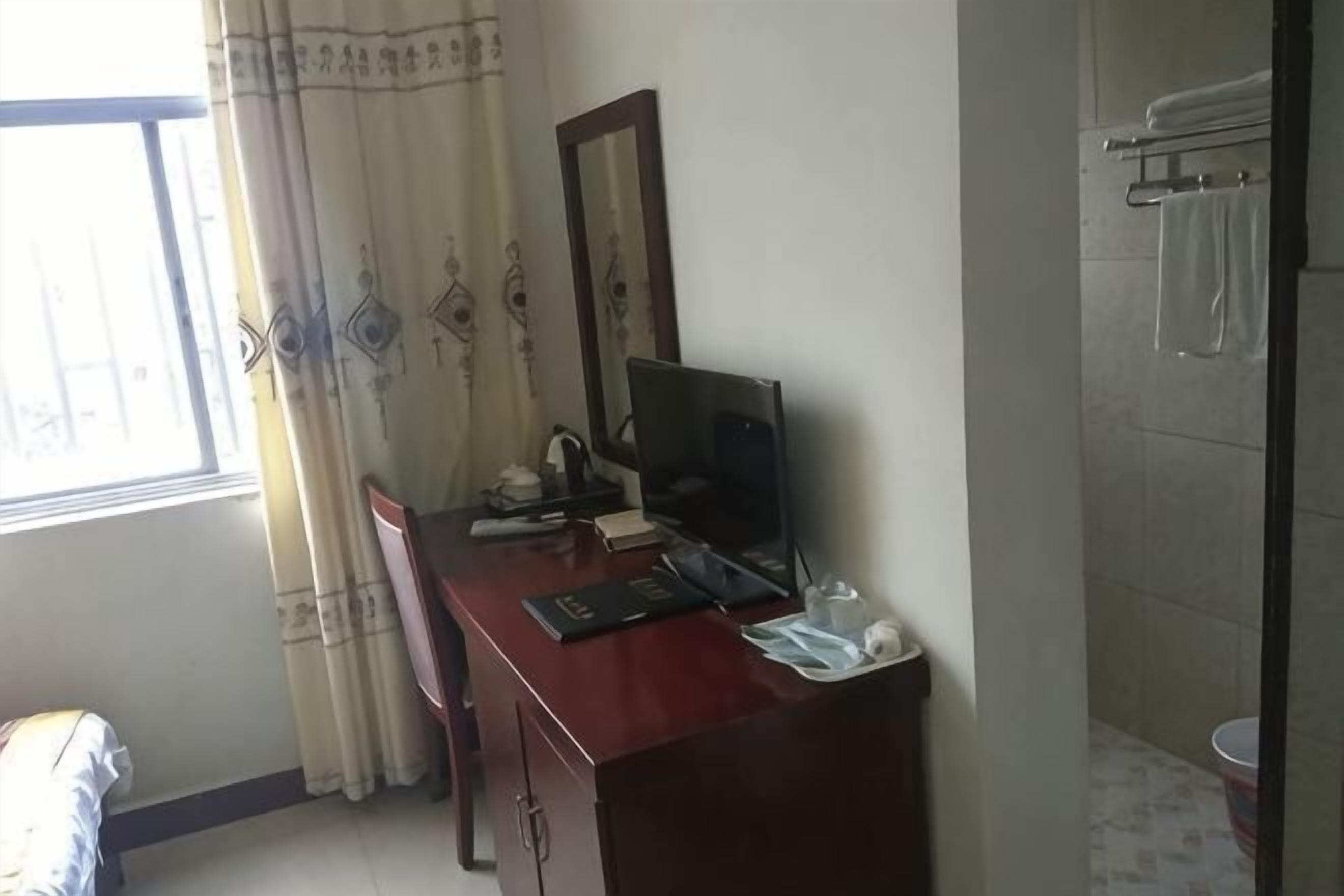 Een kamer met een bureau, computer en raam met gordijnen.
