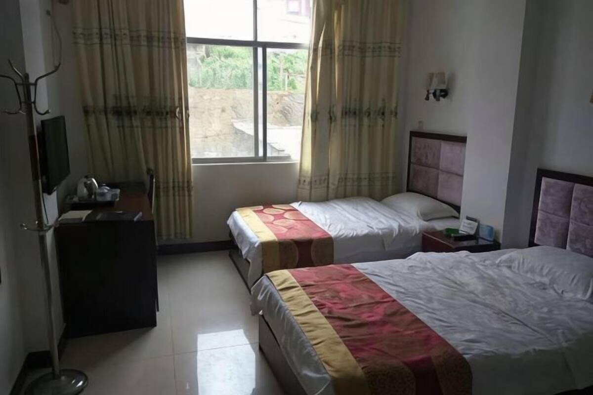 Een hotelkamer met twee bedden, een bureau, een televisie en een raam met gordijnen.