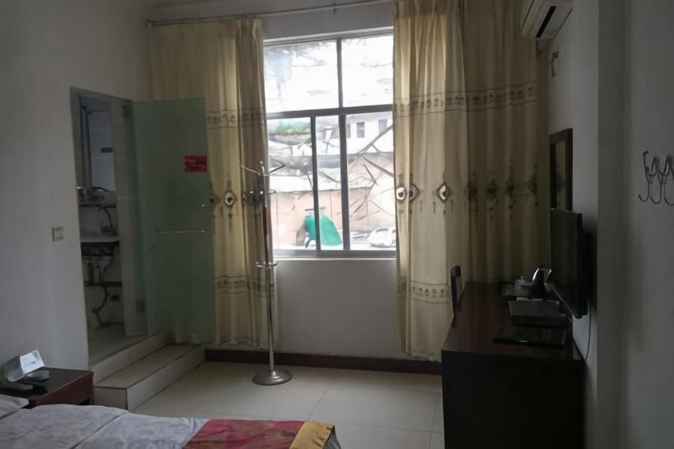 A hotel room with a bed, a desk, a chair, a window with curtains, a wardrobe, and a television.