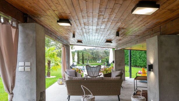 An outdoor patio with a wooden ceiling, wicker furniture, and a view of a garden. - Apartment Giada by Interhome (Castell' Alfero)