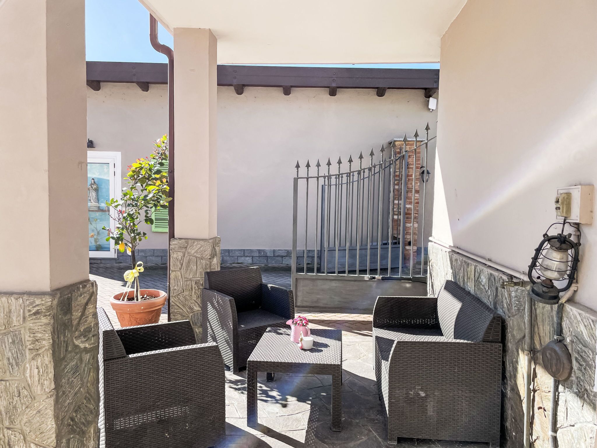 An outdoor patio with wicker furniture, a potted plant, and a metal gate.