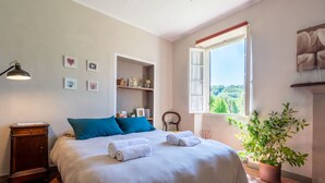 Een slaapkamer met een bed, nachtkastje, bureau, raam met uitzicht en een kamerplant.