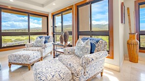 Amplia habitación con ventanas grandes que ofrecen vista a un paisaje verde. Hay dos sofás y una mesita con jarrones decorativos.