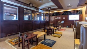 A hotel lobby with wooden paneling, seating areas, and a projection screen displaying a price. - Asahi Sauna Capsule Inn Hirosaki (Hirosaki)