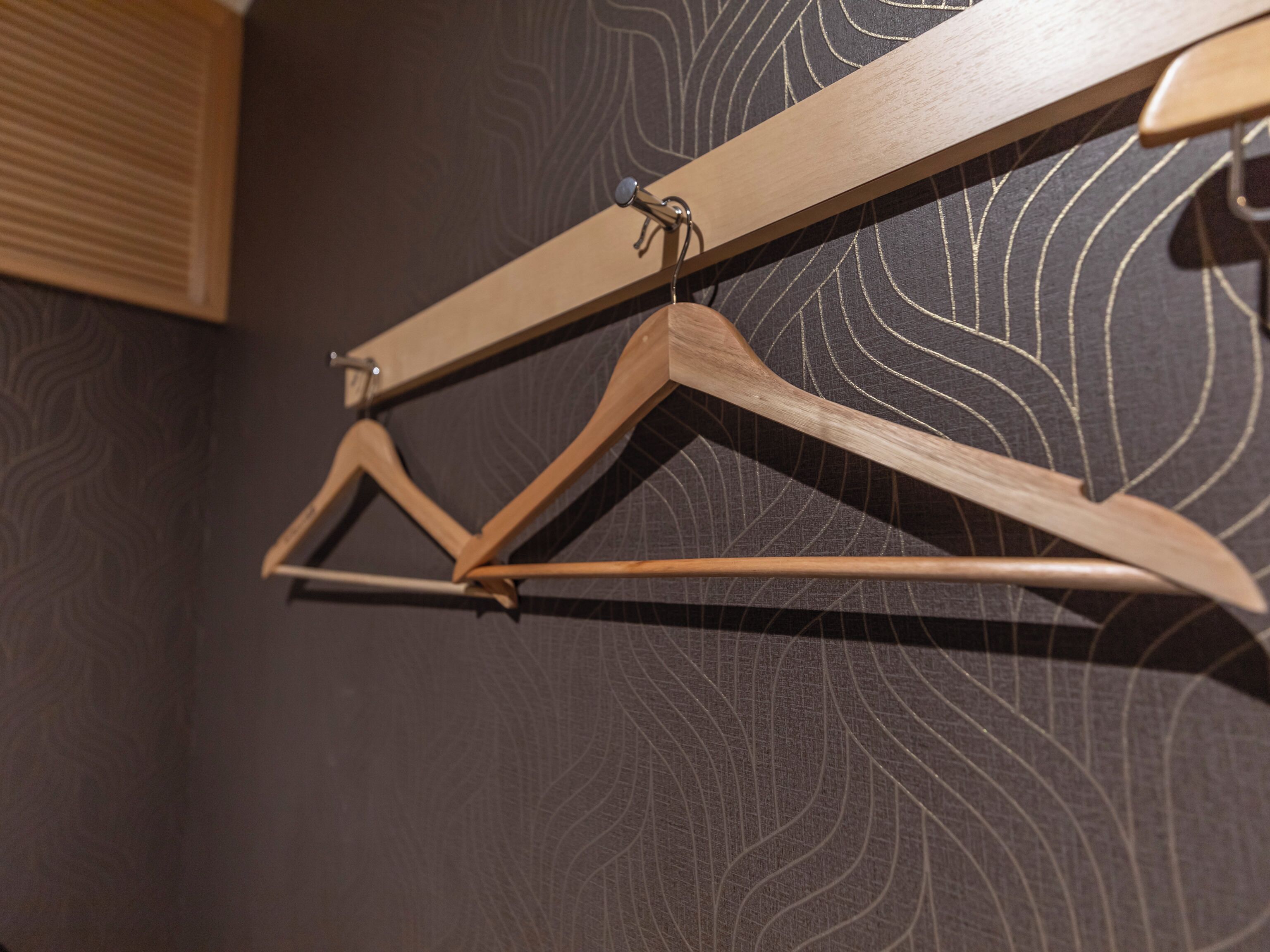 A wooden coat rack with a simple design, mounted on a wall with a textured pattern.