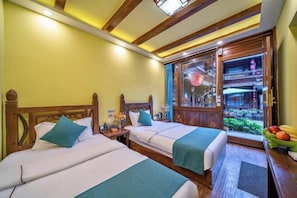 Une chambre d’hôtel avec deux lits, des têtes de lit en bois, une fenêtre donnant sur l’extérieur et une petite table avec des fruits.