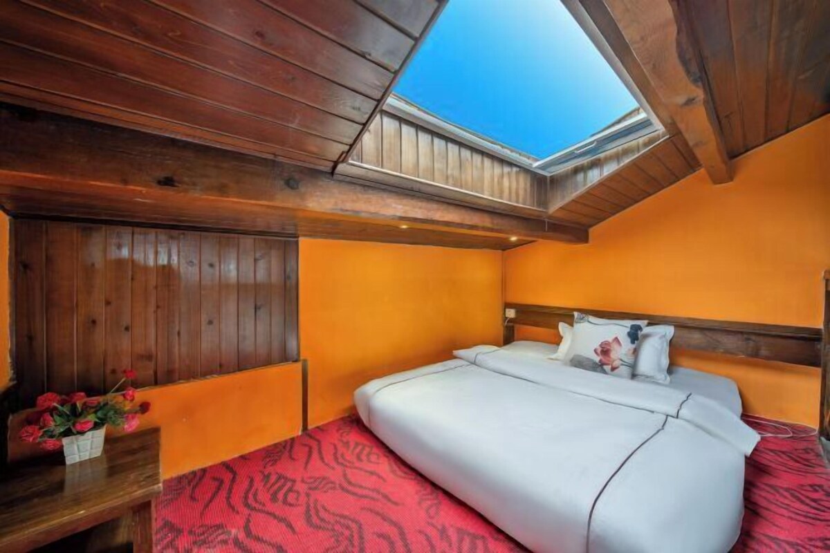 A bedroom with a wooden ceiling, a skylight, a bed with white bedding, and a red patterned rug.