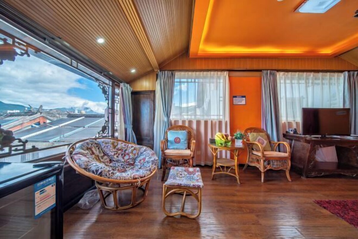 A room with a large window, wicker furniture, a small table with fruit, and a television.