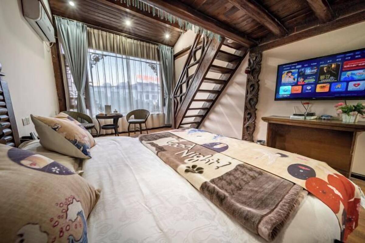 Un dormitori amb un llit, televisió, escala i finestra amb cortines.