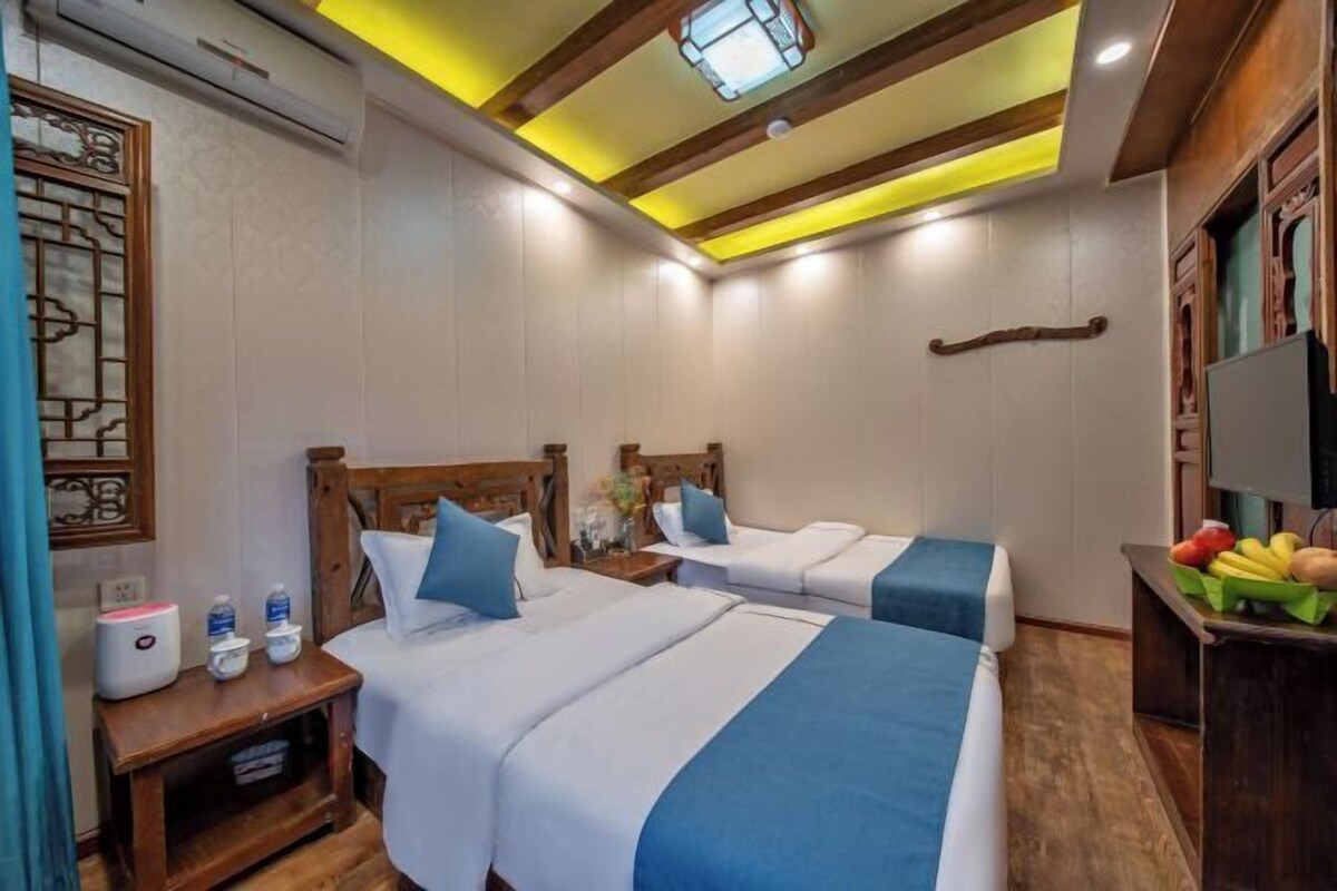 A hotel room with two beds, a wooden headboard, a small table with a fruit basket, and a TV on a wooden stand.