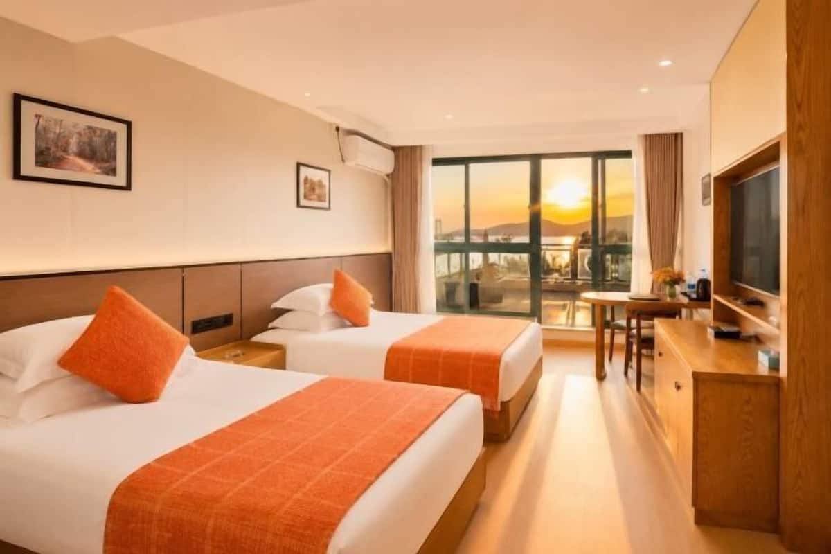 Ein Hotelzimmer mit zwei Betten, einem Fernseher, einem Schreibtisch und einem großen Fenster mit Blick auf die Stadt.