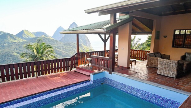 A pool area with a view of mountains, a covered deck with wicker furniture, and a wooden railing. - Piton Villa Deck.. Million View of Majestic Pitons (Soufrière)
