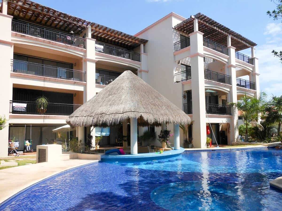 A hotel with a swimming pool, a thatched-roof structure, and multiple balconies.