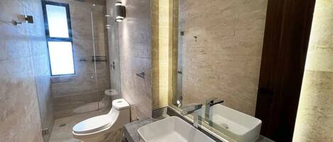 A modern bathroom with a toilet, a large sink, and a glass-enclosed shower.