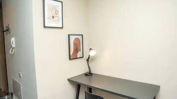 Quarto com escrivaninha, duas obras de arte emolduradas, luminária de mesa e uma cadeira.