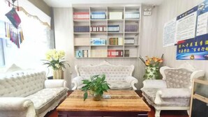 A living room with a bookshelf, two white sofas, a coffee table, and a decorative plant. - Xinlong Hotel (Baojing)