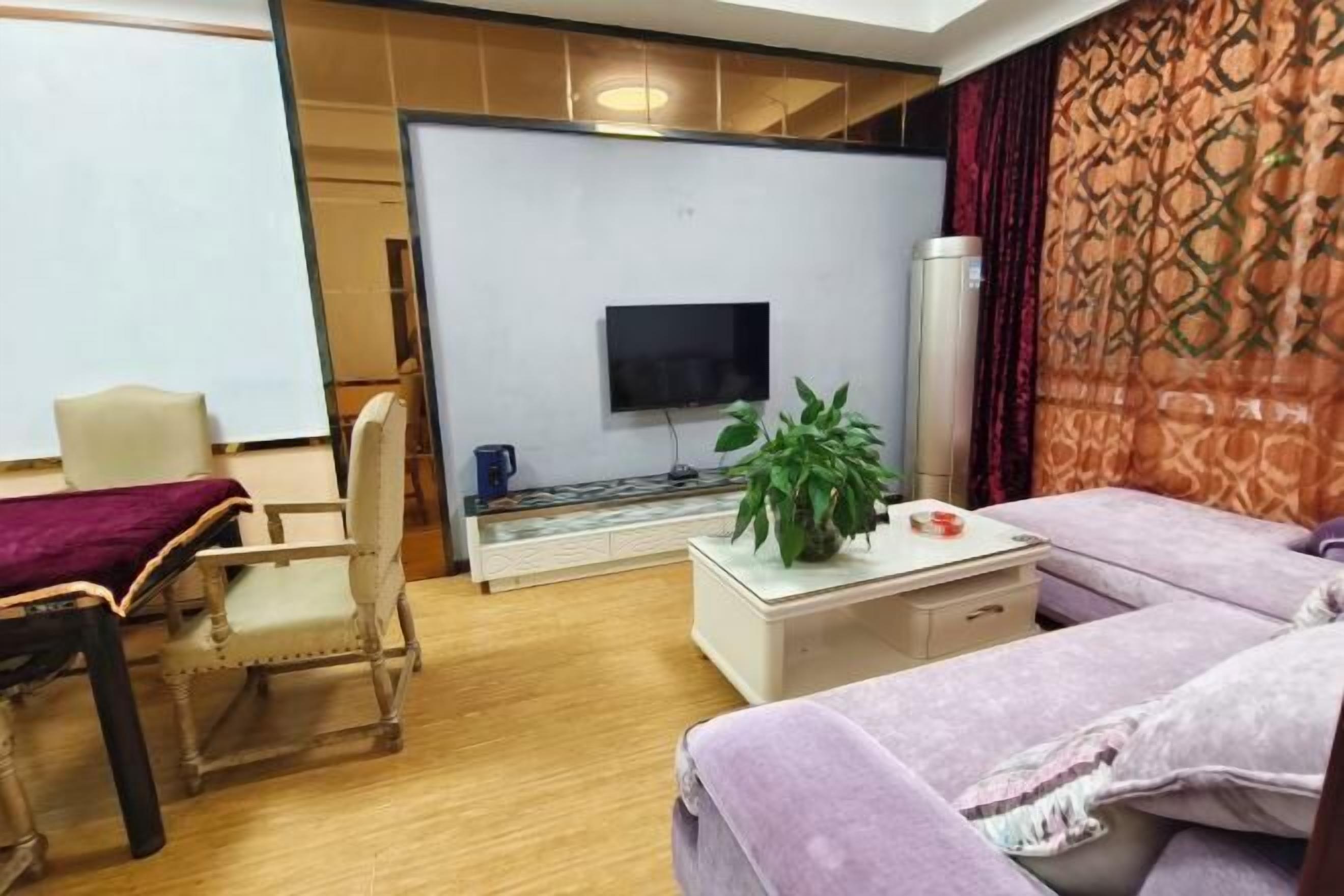 A room with a television, a plant, a sofa, a chair, and a coffee table.