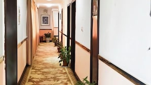 A hotel hallway with patterned carpet, potted plants, and doors leading to rooms. - Xinlong Hotel (Baojing)