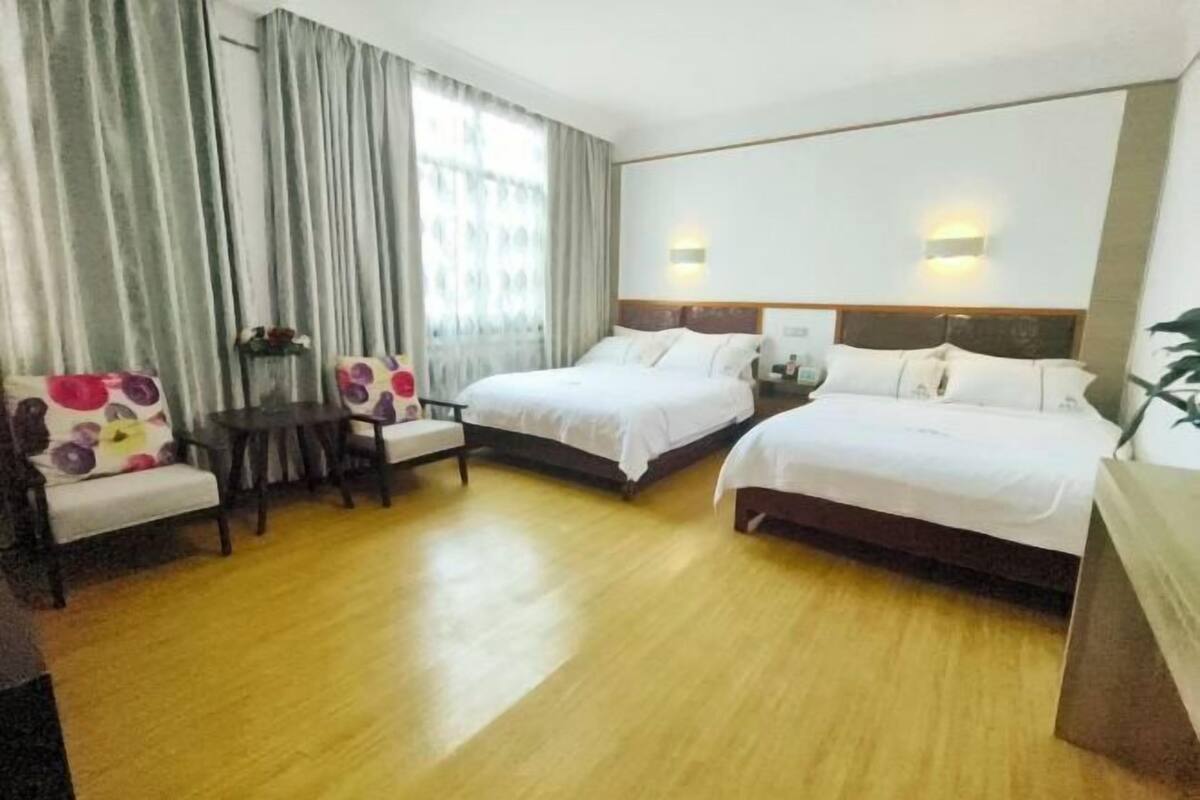 A hotel room with two beds, a small table, a chair, and a large window with curtains.