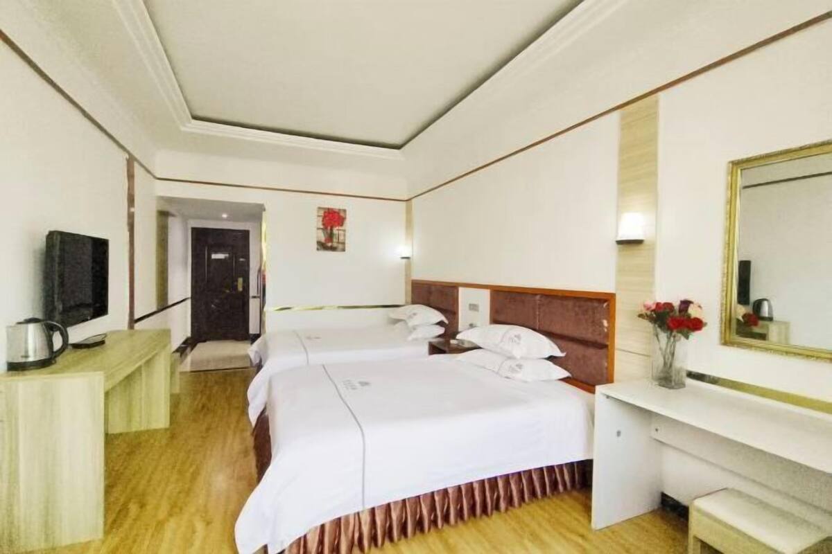 A hotel room with two beds, a television, a desk, and a mirror.