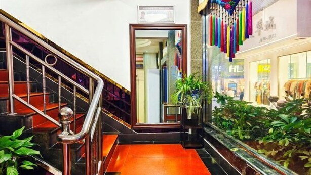 A staircase with metal railings and a red-tiled floor, leading to a door with a framed picture above it. - Xinlong Hotel (Baojing)