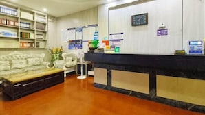 A reception area with a reception desk, a sofa, a bookshelf, and a clock on the wall. - Xinlong Hotel (Baojing)