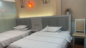A hotel room with two single beds, a nightstand, a chair, and a wall-mounted lamp. - Xinlong Hotel (Baojing)