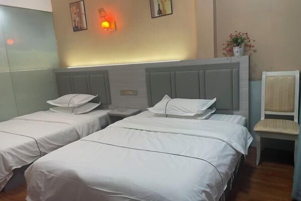 Une chambre d’hôtel avec deux lits simples, une table de chevet, une chaise et une lampe fixée au mur.