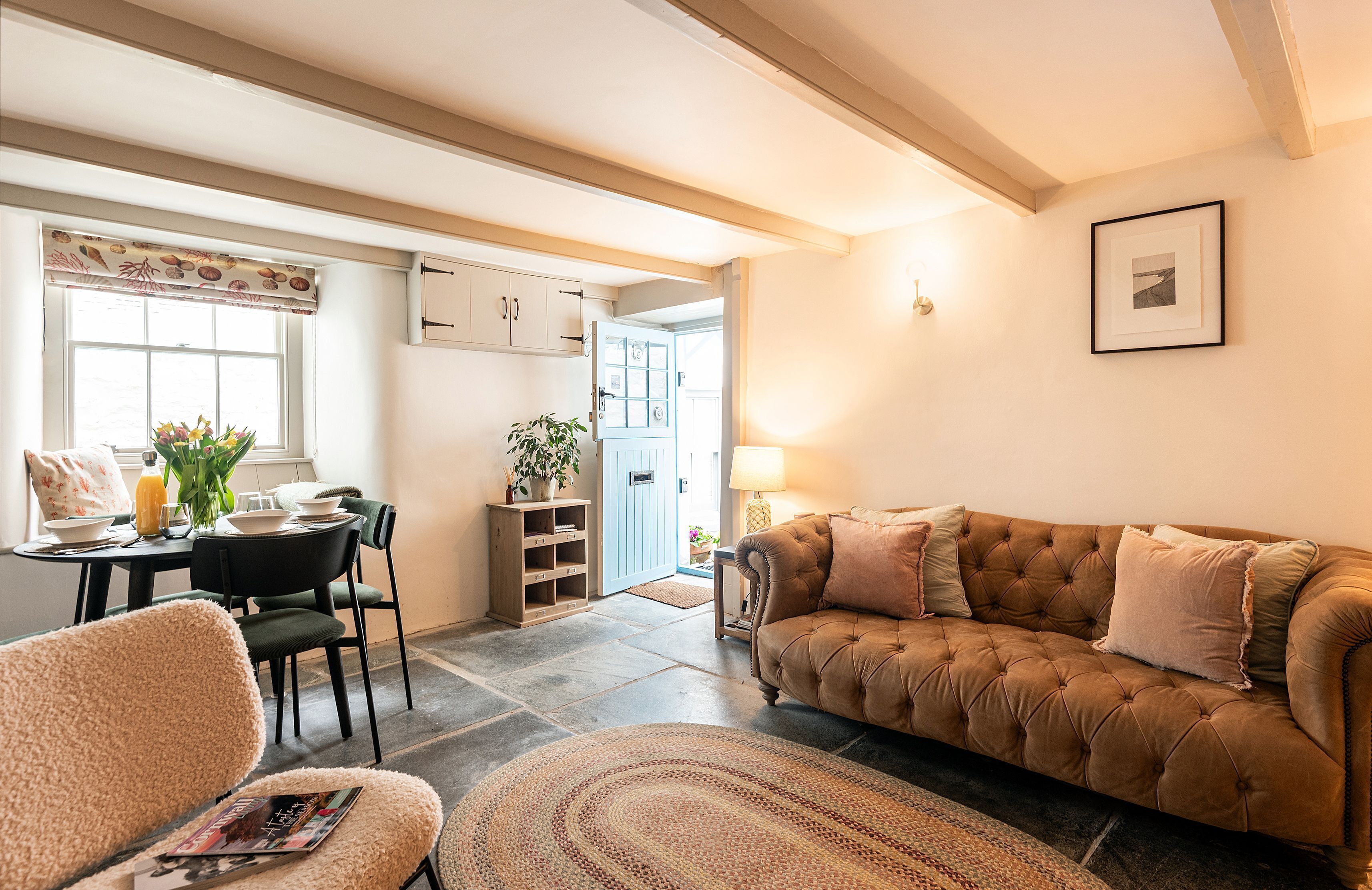 A cozy living room with a brown sofa, a dining table with chairs, and a kitchen area in the background.