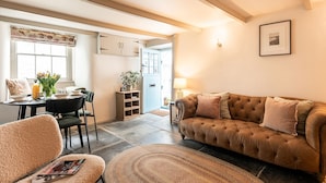 En hyggelig stue med en brun sofa, et spisebord med stole, og et køkken i baggrunden.