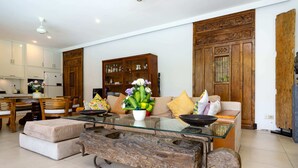 A modern living room with a glass coffee table, a wooden cabinet, and a sofa with cushions. - Villa Mangga (Legian)
