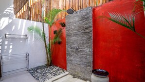 A small, enclosed outdoor area with a red wall, a bamboo fence, a metal towel rack, and a potted plant. - Villa Mangga (Legian)