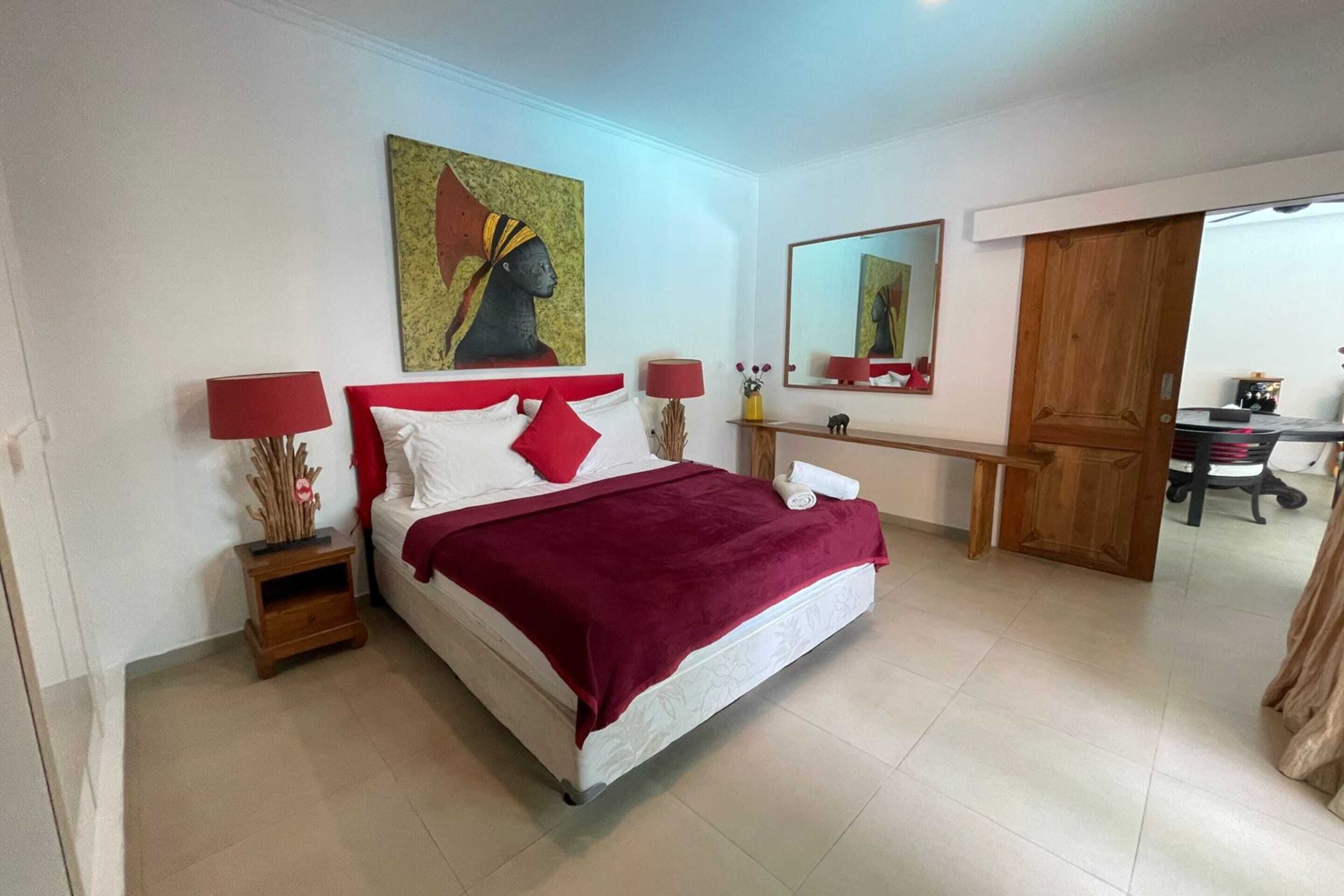 A bedroom with a bed, two bedside tables, a nightstand, a mirror, and a wooden door.